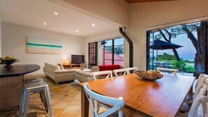 A spacious living area with a wooden dining table, white chairs, a sofa, and a television. - Panoramic Bay Views - Pet friendly & only a  5 minute stroll to town (Dunsborough)