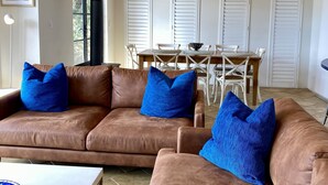 A modern living room with two brown leather sofas, a dining table with chairs, and a staircase with black railings. - Panoramic Bay Views - Pet friendly & only a  5 minute stroll to town (Dunsborough)