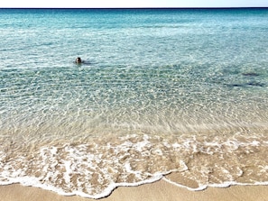 A beach with clear water and a person swimming.