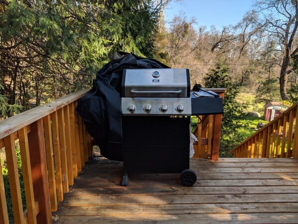Una parrilla portátil sobre una terraza de madera con vista a árboles y un cielo despejado.