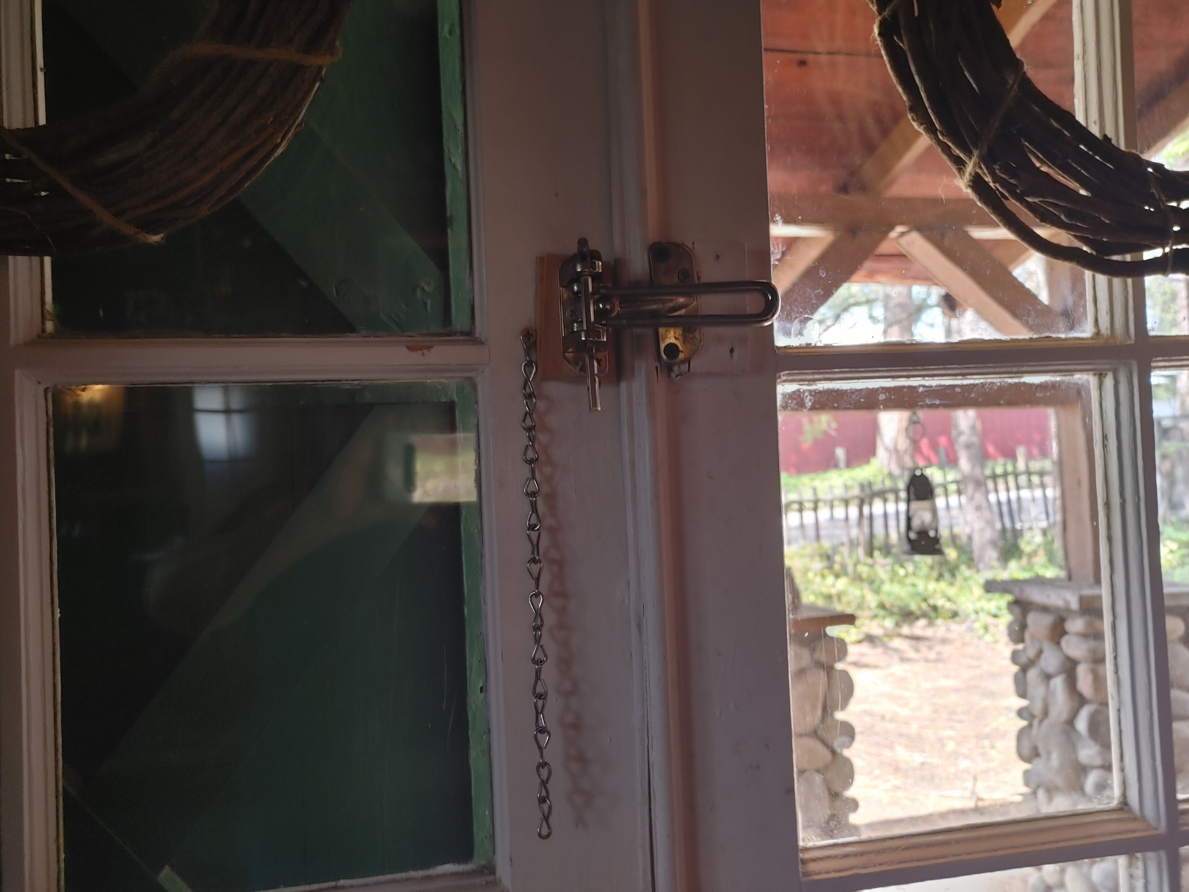 A partially open door with a chain lock, a green window, and a view of an outdoor area with a fence and a lantern.