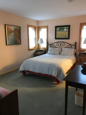 Un dormitorio con una cama, dos mesitas de noche, una silla y dos ventanas.