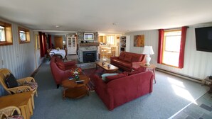 A spacious living room with a fireplace, red sofas, a coffee table, and a dining area in the background. - Slow down…You’re on Island Time (Isle La Motte)