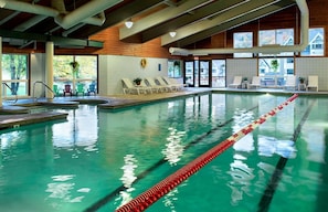 An indoor swimming pool with clear lane dividers, lounge chairs, and a view of the outside through large windows. - Luxury Home On Loon Mtn Home,  Spectacular Mountain Views, Pool/Spa access incl (Lincoln)