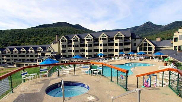 A hotel with multiple buildings, a swimming pool, and a mountain backdrop.