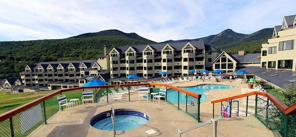 A hotel with multiple buildings, a swimming pool, and a mountain backdrop.