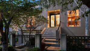 Un bâtiment moderne avec un escalier menant à une porte, le tout entouré d’une clôture métallique et de verdure.