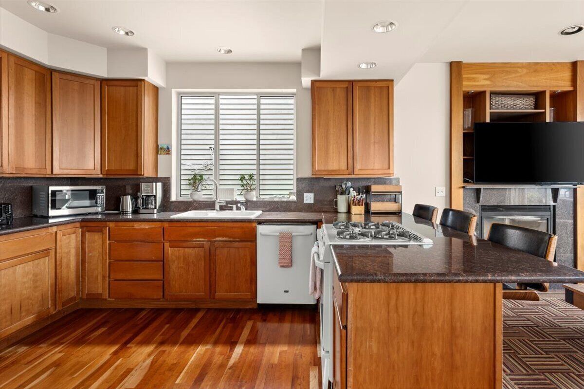Une cuisine moderne avec des meubles en bois, des appareils en acier inoxydable, un grand îlot central et un téléviseur à écran plat.