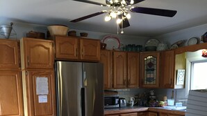 Eine Küche mit Holzschränken, einem Edelstahlkühlschrank, Holzbarhocker, einem Deckenventilator und einer gefliesten Spritzschutzwand.