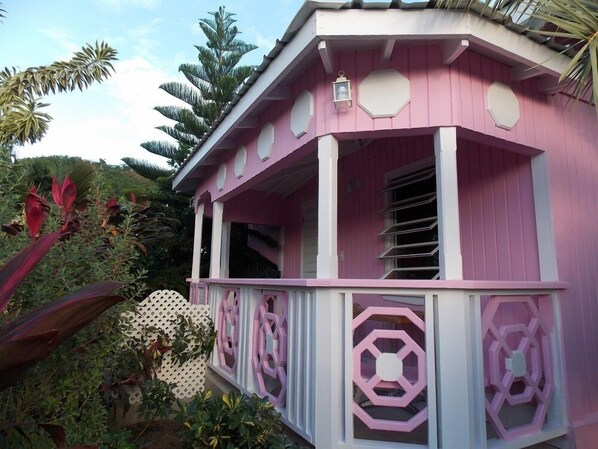 A pink building with a balcony, surrounded by tropical plants.