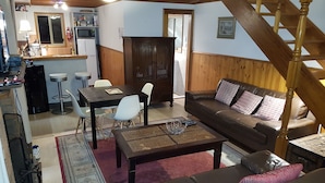 En hyggelig stue med en lædersofa i brunt, et spisebord med stole, et køkken med mikroovn og køleskab, samt en trappe i træ.