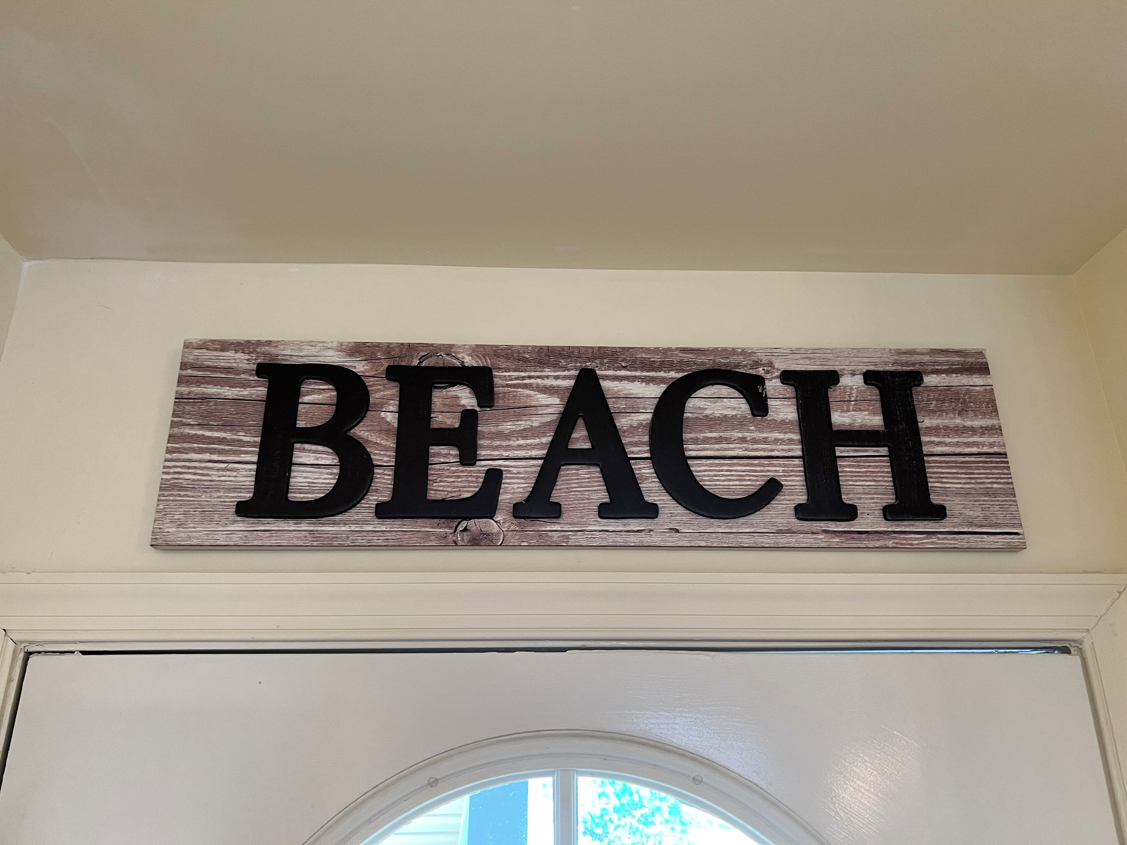 Une enseigne en bois portant le mot « PLAGE » est fixée au mur au-dessus d’une porte.