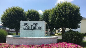 A sign for 'The Palms' with a fountain and pink flowers in the foreground. - Spacious Condo with Pool Near Beach- New Floors and Furniture!  (Rehoboth)