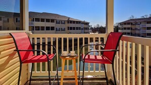A balcony with two red chairs and a small table with cups, overlooking a row of multi-story buildings. - Spacious Condo with Pool Near Beach- New Floors and Furniture!  (Rehoboth)