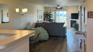 A spacious living room with a gray sofa, a dining area with a table and chairs, a large plant, and a ceiling fan. - Spacious Condo with Pool Near Beach- New Floors and Furniture!  (Rehoboth)