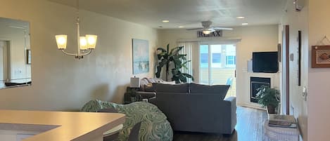 En rummelig stue med en grå sofa, et spisebord med stole, en stor plante og en ventilator i loftet.