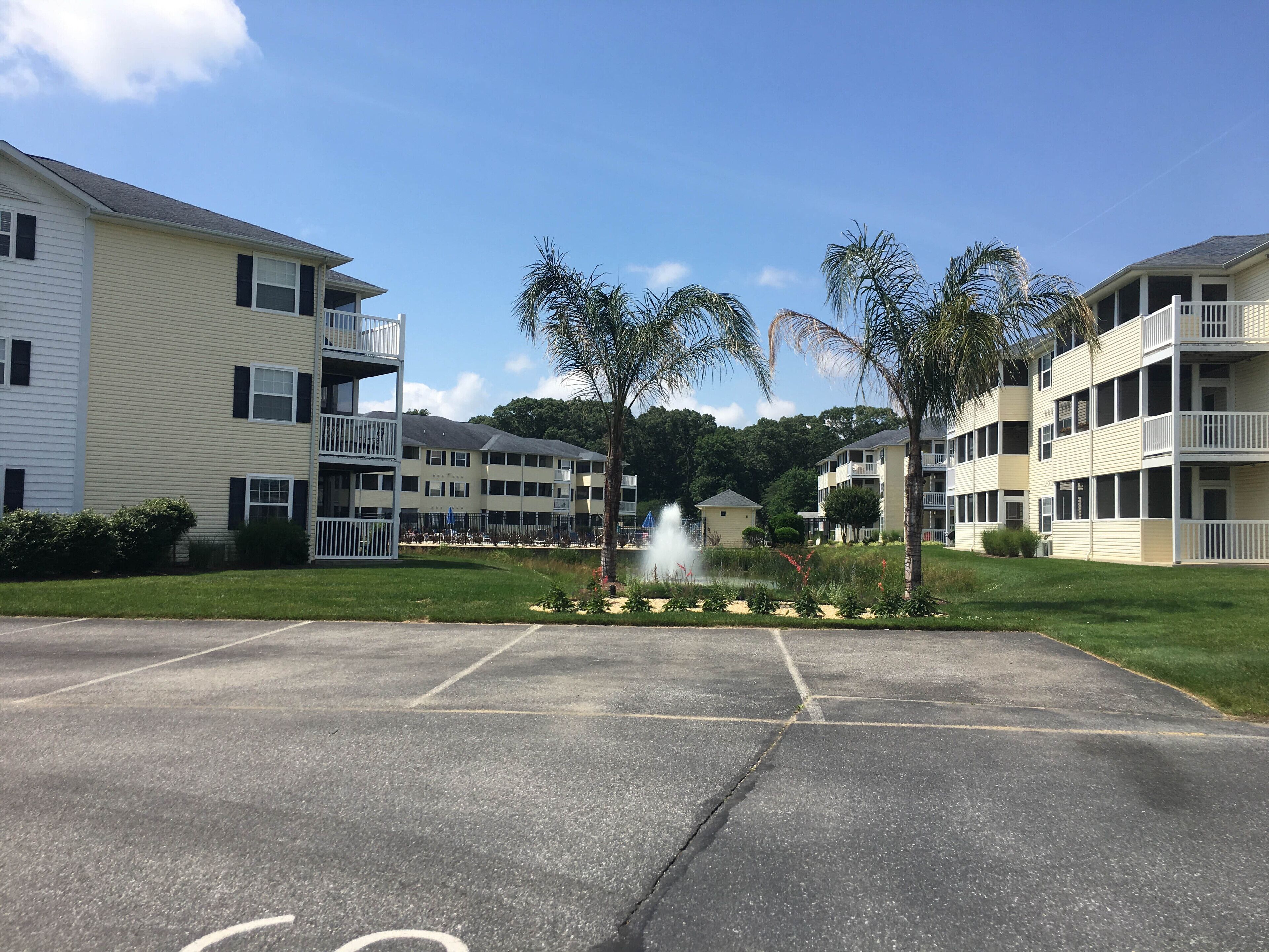 A multi-story residential building with balconies, a parking lot, and a fountain.