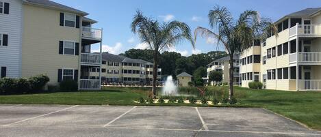 A multi-story residential building with balconies, a parking lot, and a fountain.