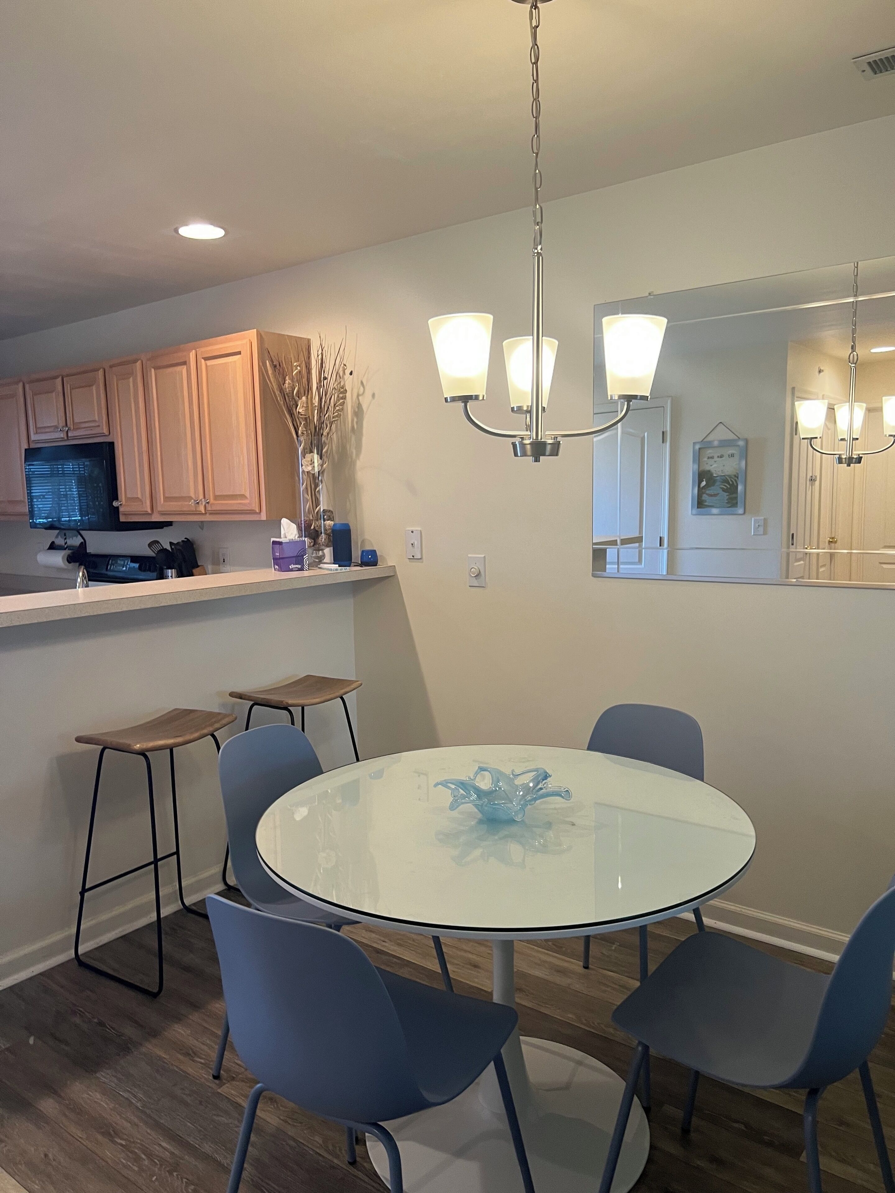 A modern kitchen with wooden cabinets, a microwave, and a dining area with a glass table and blue chairs.