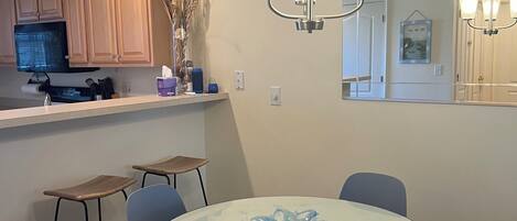 A modern kitchen with wooden cabinets, a microwave, and a dining area with a glass table and blue chairs.