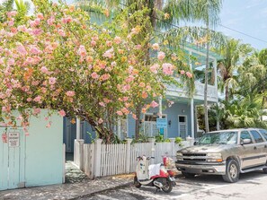 A building with a white picket fence, a parked scooter, and a vehicle on the street.