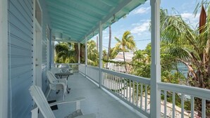 A covered porch with white chairs and a table, overlooking a tropical landscape with palm trees and a beach. - STEPS TO DUVAL, OLD TOWN!  'LA DOLCE VITA'  #6, SLEEPS 2-4, 3  BLKS TO STH BCH (Key West)