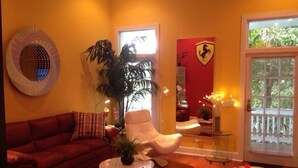 A living room with a red sofa, a white armchair, a round coffee table, and a potted plant. - STEPS TO DUVAL, OLD TOWN!  'LA DOLCE VITA'  #6, SLEEPS 2-4, 3  BLKS TO STH BCH (Key West)