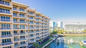 A multi-story hotel with balconies, a marina with boats, and a clear view of the water. - Harborview Grande, Clearwater Beach - Private Balcony, Walk to It All (Clearwater Beach)