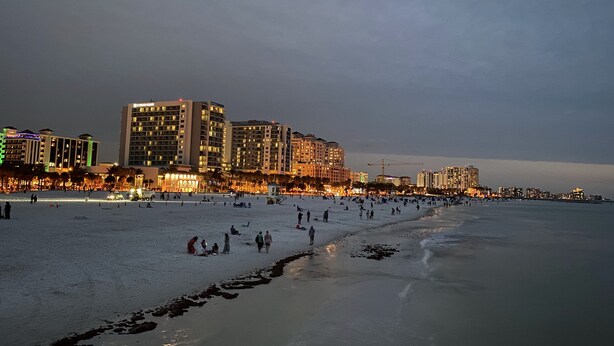 A beach with people walking and sunbathing, and buildings in the background. - Harborview Grande, Clearwater Beach - Private Balcony, Walk to It All (Clearwater Beach)