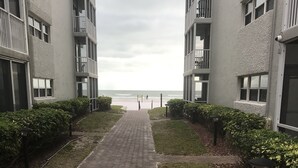 Un camino que lleva a una playa, con vistas al océano, flanqueado por edificios con balcones y una cámara de seguridad.