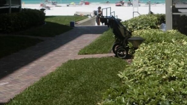 Un sendero que lleva a una playa con sombrillas y un cochecito.