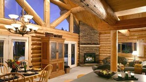 A log cabin interior with a dining area, fireplace, and large windows.