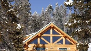 A log cabin with a balcony, surrounded by snow-covered trees.