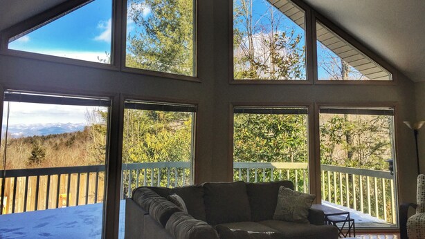 A room with a large window overlooking a snowy landscape, a wooden deck, and a cushioned seating area. - Perfect for Large Groups • Hot Tub • Fire Pit • Fast Wi-Fi & Sparkling Clean (Pisgah Forest)