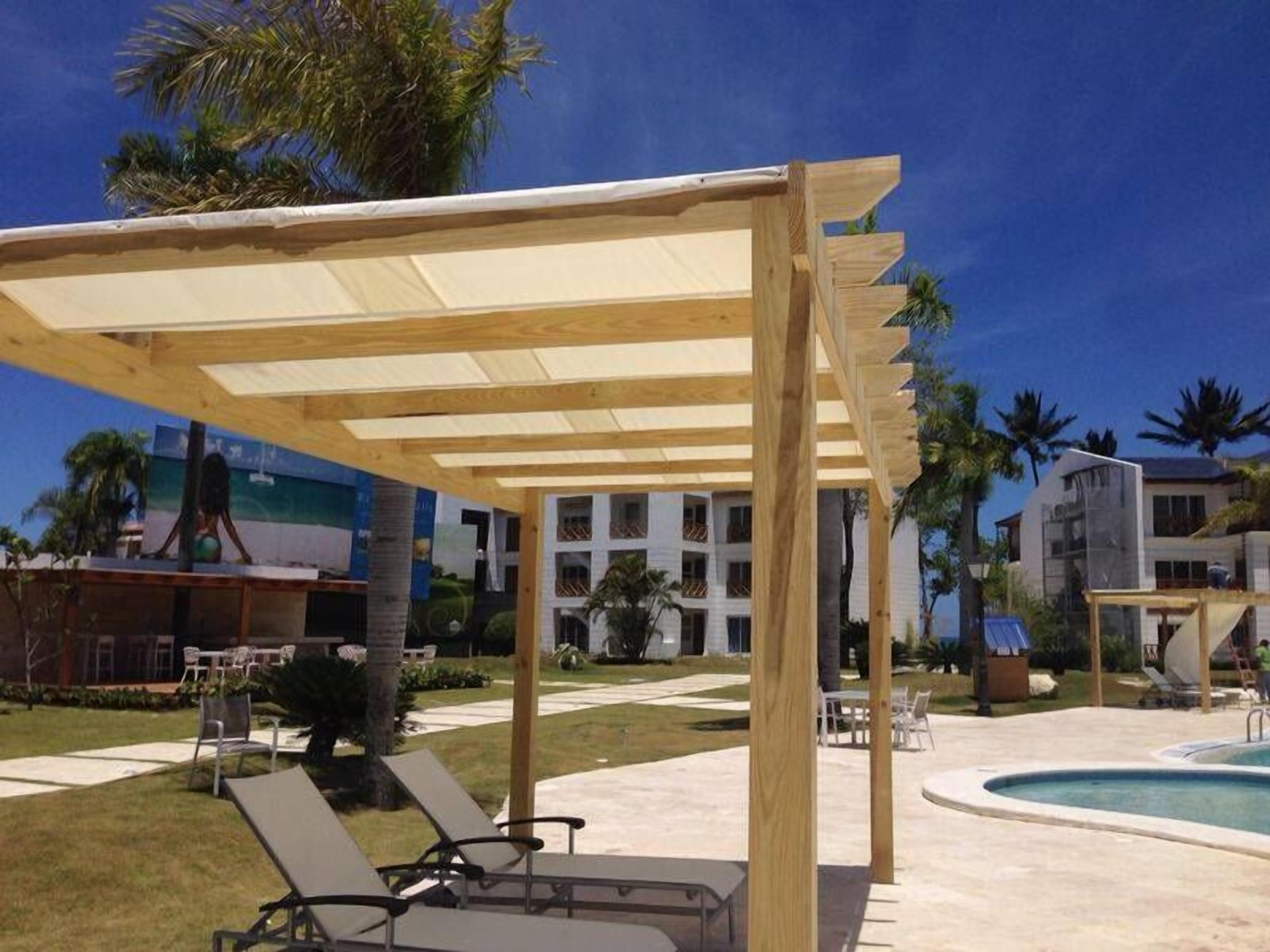 Zona junto a la piscina con una pérgola de madera, sillas de descanso y una alberca.