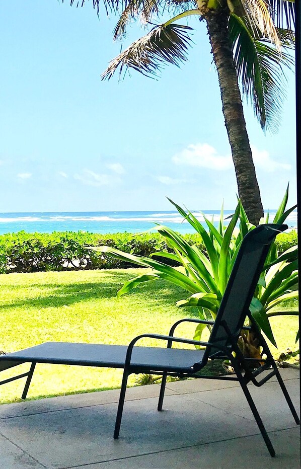 A lounge chair on a concrete surface with a view of the ocean and palm trees.