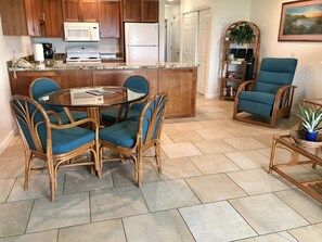 Una cocina con armarios de madera, microondas, refrigerador y un comedor con sillas de mimbre y una mesa de vidrio.