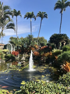 A serene garden with a central fountain, surrounded by palm trees and lush vegetation. - Pono Kai Resort Kaua'i Beach-Front Condo (Kapaa)