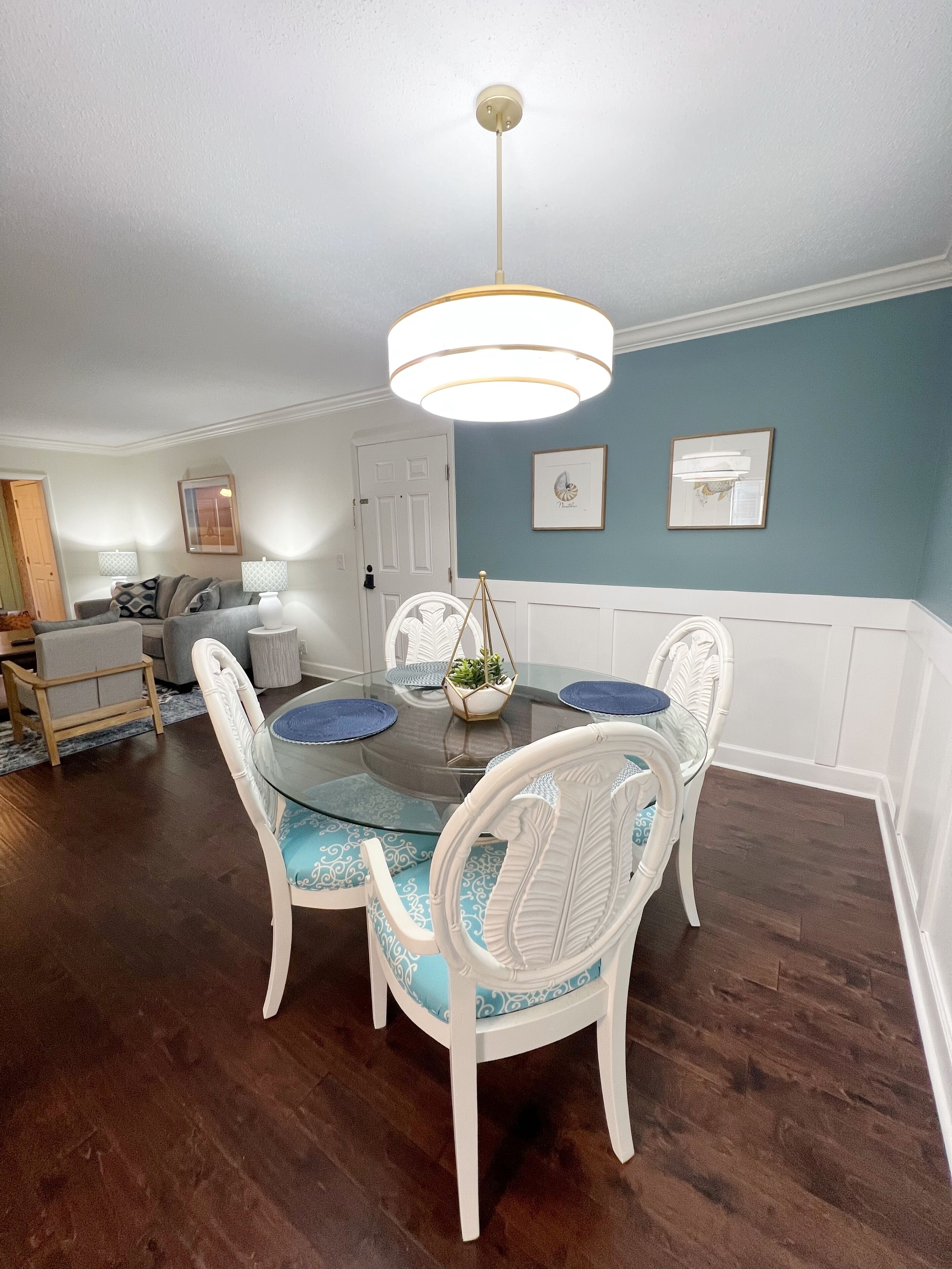 Un coin repas avec une table à plateau en verre, des chaises blanches et un luminaire suspendu.