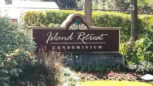 Une enseigne indiquant le complexe de condominiums « Island Retreat », entourée de verdure et se dressant sous un ciel dégagé.