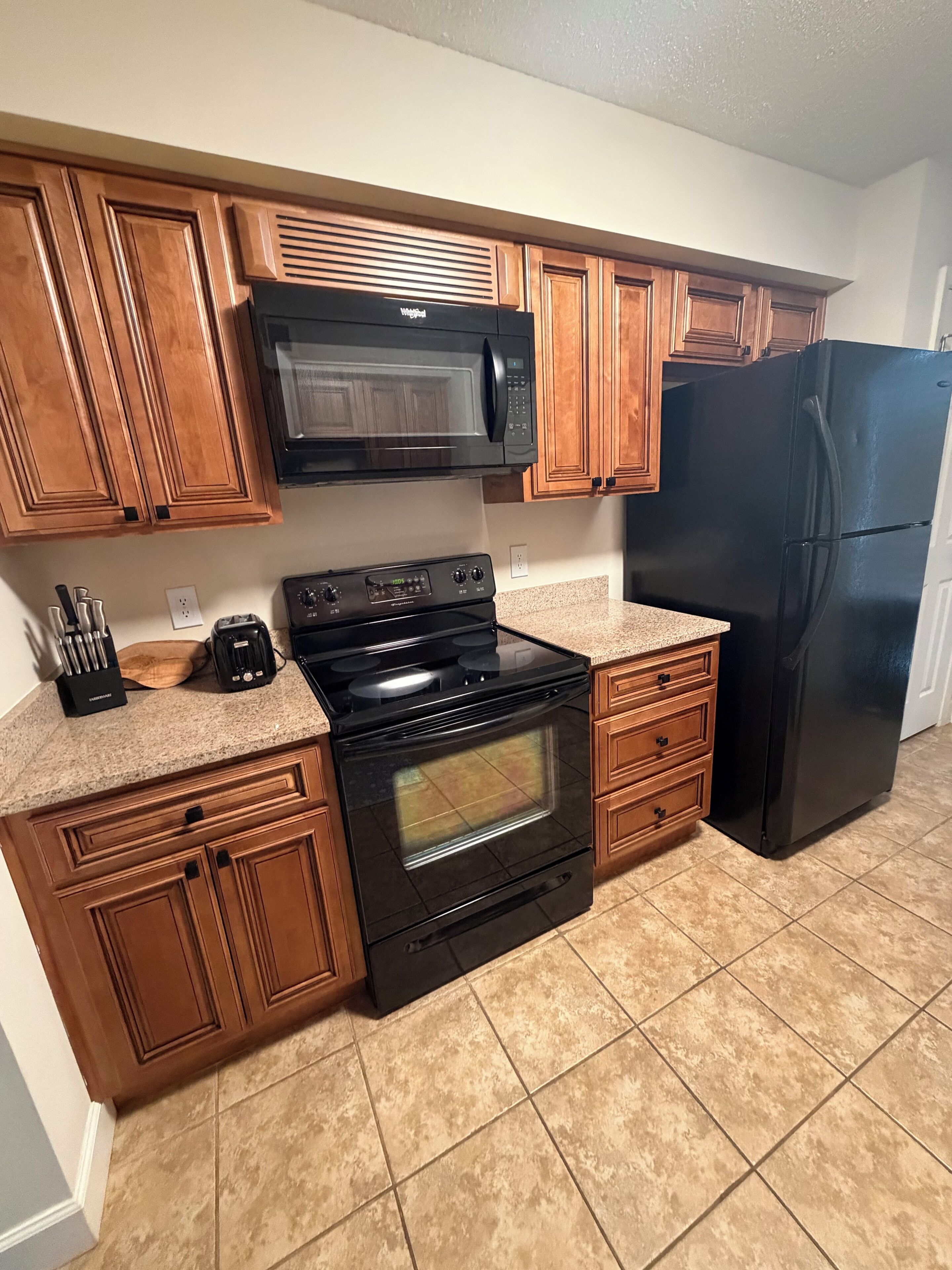Une cuisine avec des meubles de rangement en bois, une cuisinière noire, un four à micro-ondes et un réfrigérateur noir.