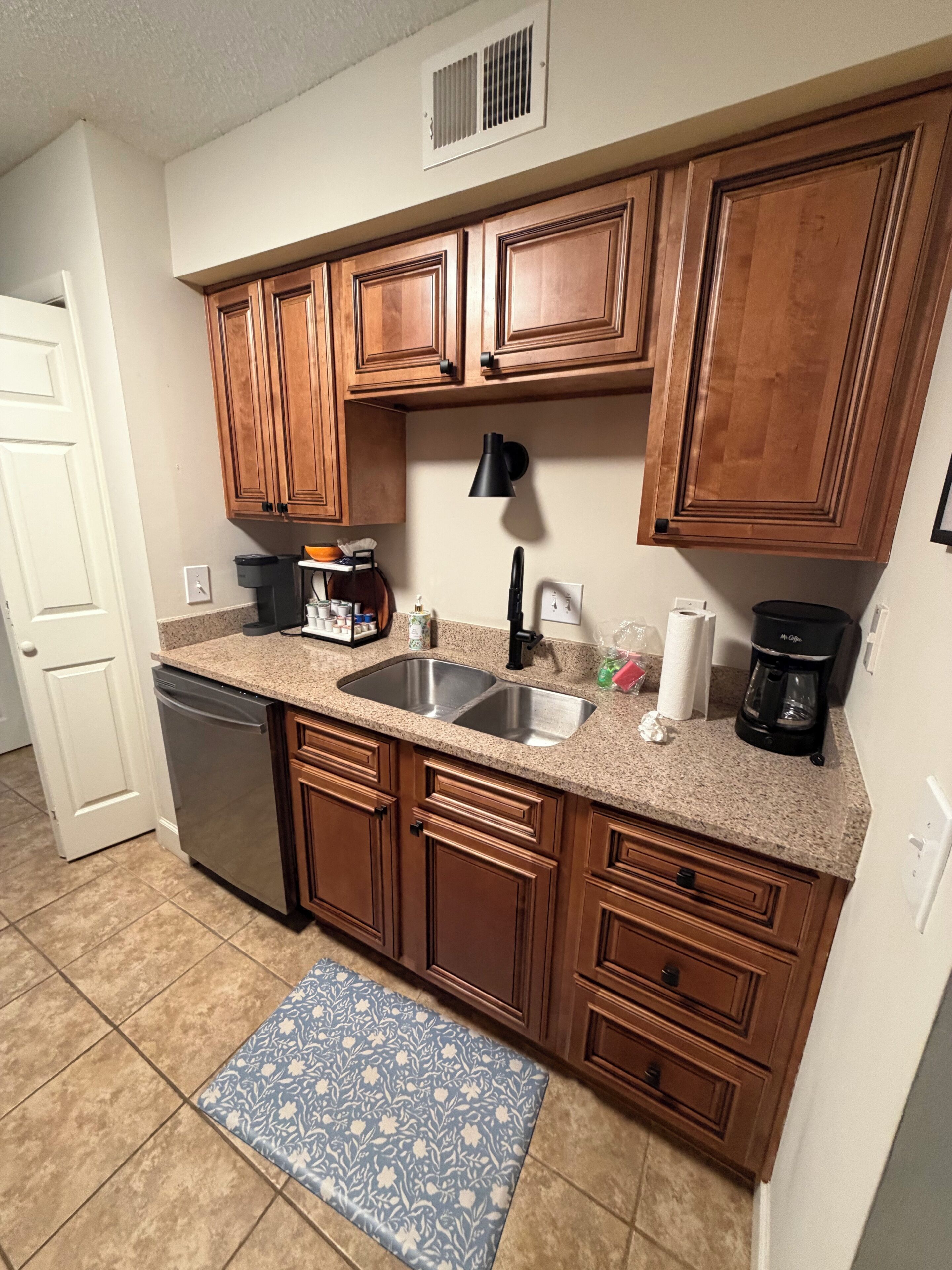 A kitchen with wooden cabinets, a stainless steel sink, a coffee maker, and a dishwashing machine.