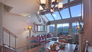 A spacious living area with a wooden dining table set for two, a sofa, and a large window offering a mountain view. - Gorgeous Ski Mountain Views 2 Bedroom, 2 Bath - Ski In Out Condo at Beaver Run (Breckenridge)