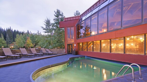 A modern building with a swimming pool, lounge chairs, and a forested background. - Gorgeous Ski Mountain Views 2 Bedroom, 2 Bath - Ski In Out Condo at Beaver Run (Breckenridge)
