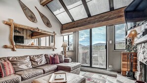 A cozy living room with a leather sofa, a wooden coffee table, and a large window offering a mountain view. - Gorgeous Ski Mountain Views 2 Bedroom, 2 Bath - Ski In Out Condo at Beaver Run (Breckenridge)