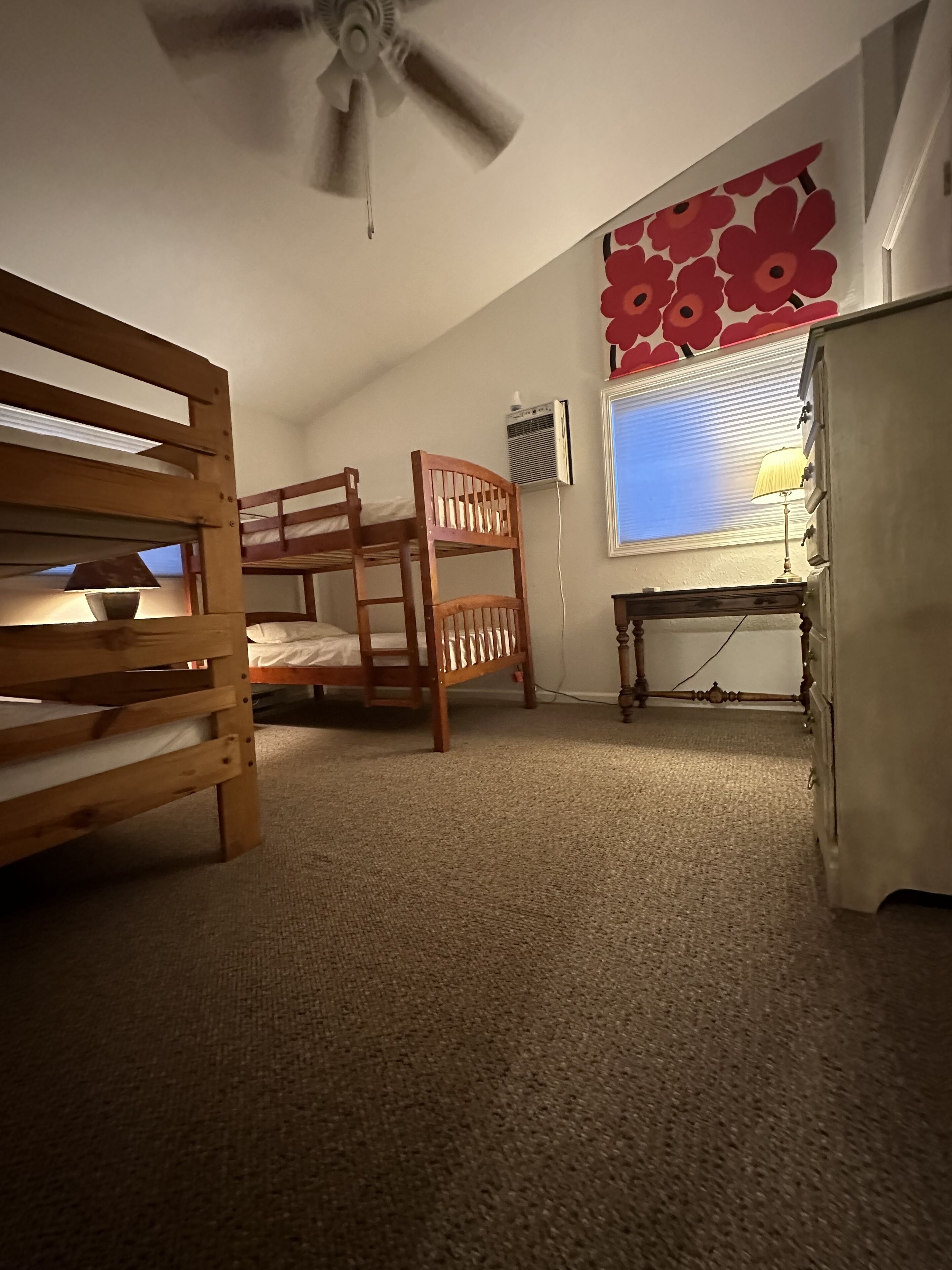 Un dormitorio con literas, un escritorio, un aparador y un ventilador de techo, además de una ventana con persianas.