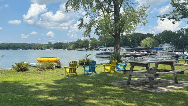 Un espacio para picnic junto al lago con una mesa de madera y sillas Adirondack de colores.