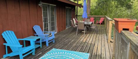 Una terraza de madera con un tapete azul estampado, mobiliario de exterior con sillas y una mesa, y una planta en maceta.