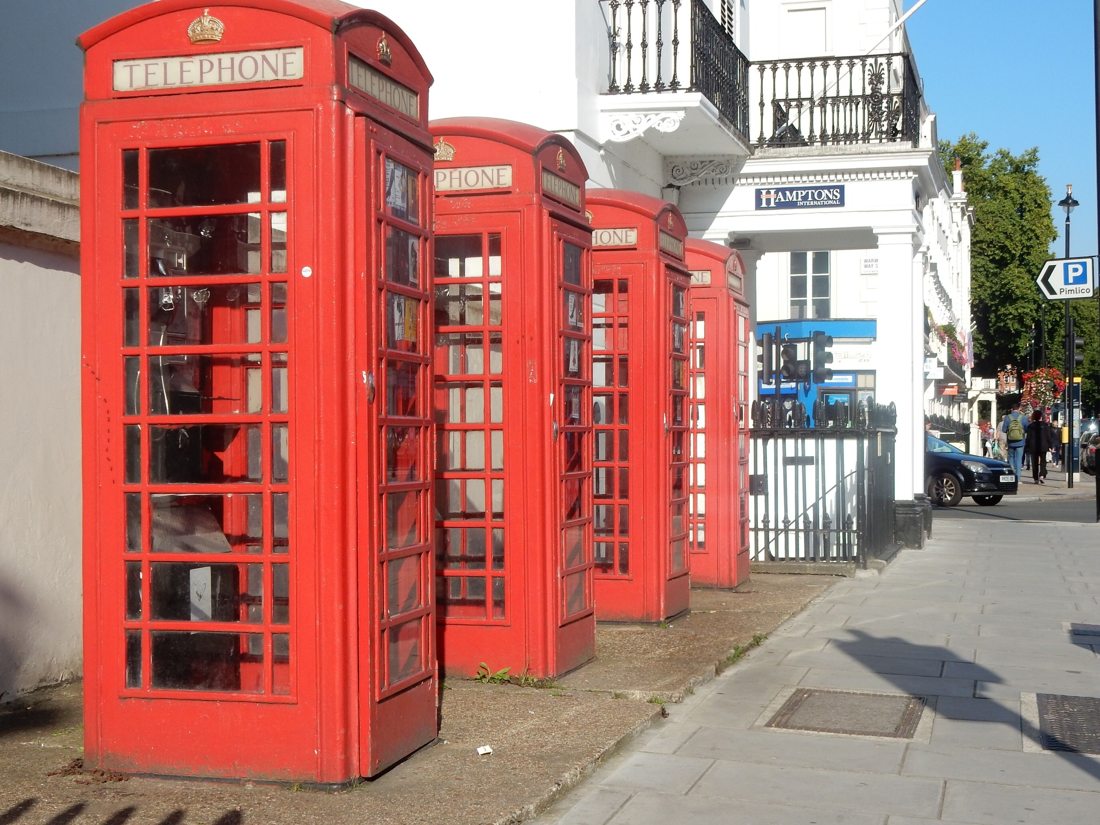A row of red telephone booths on a city sidewalk.
