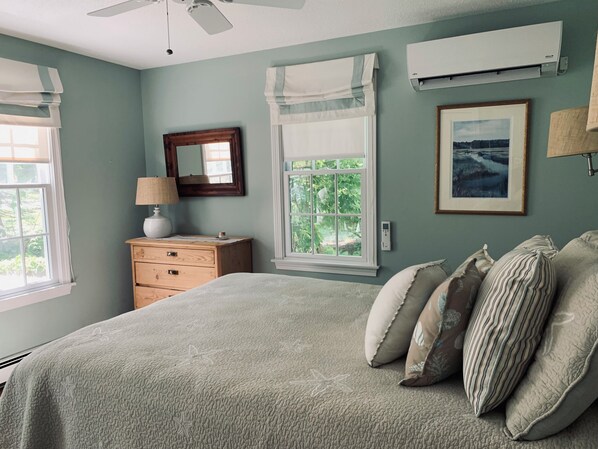 A bedroom with a bed, dresser, and two windows with curtains.